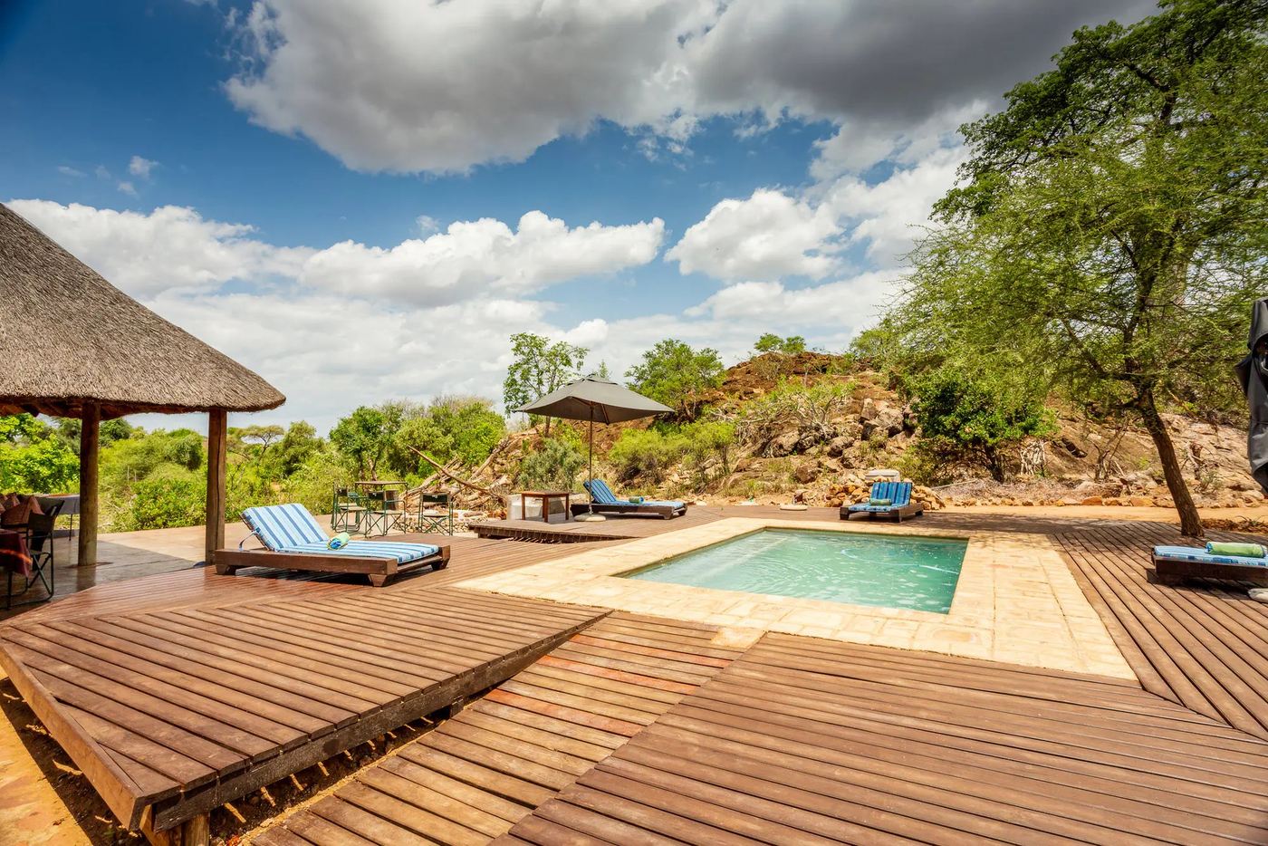 Wooden sundeck and pool with loungers under thatch gazebos at Baobab Hill House