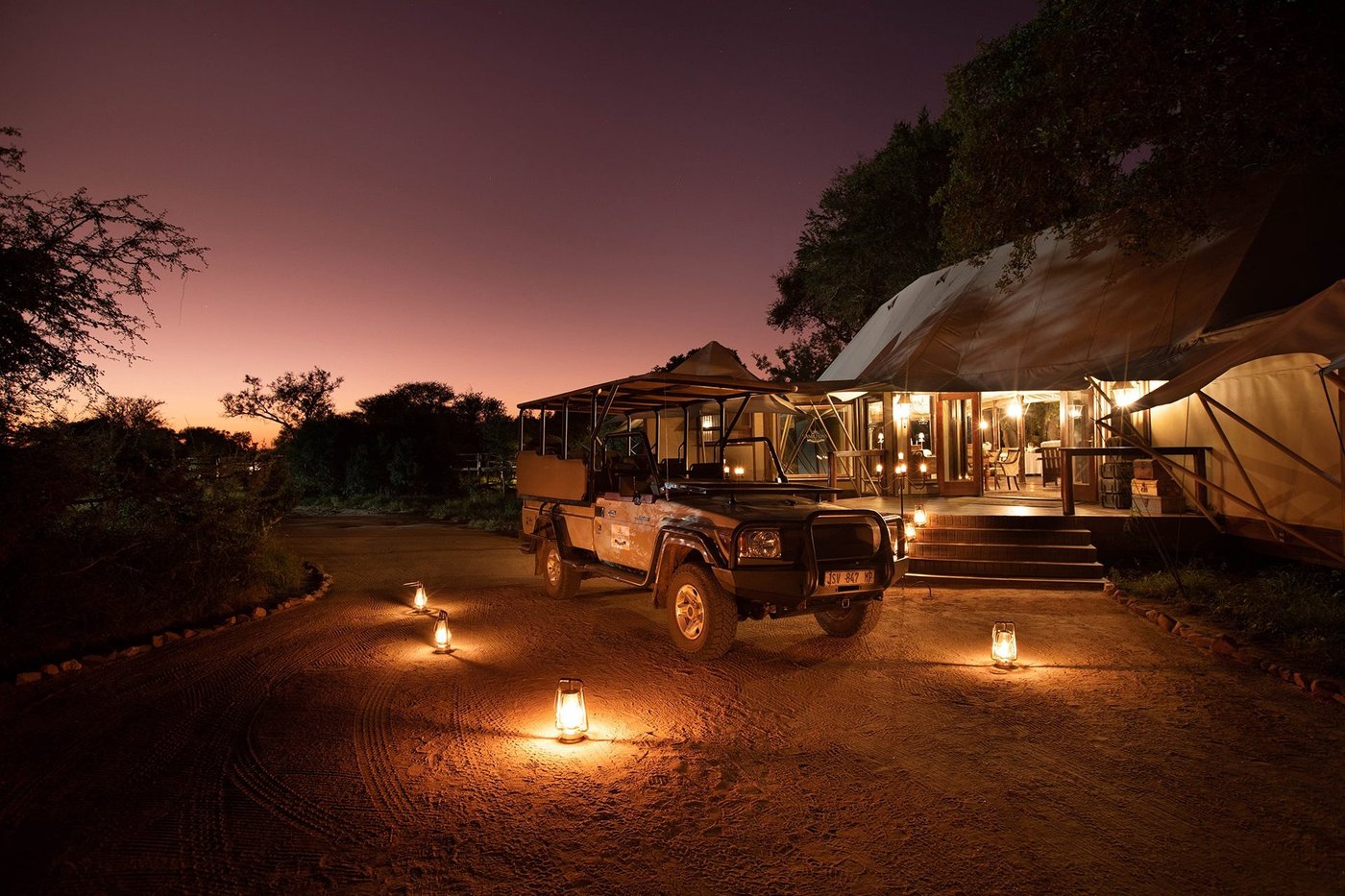 Hamiltons Tented Camp safari vehicle and lantern-lit entrance at dusk in Kruger