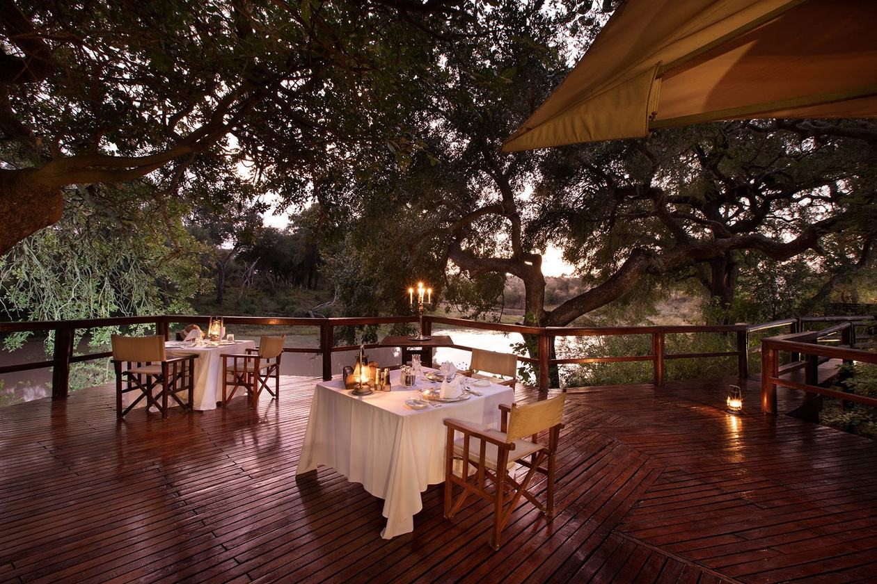 Private dining table set on the riverside deck at dusk at Hamiltons Tented Camp