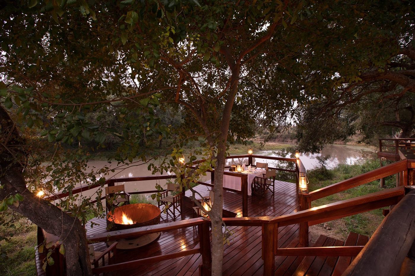 Candlelit wooden deck with loungers overlooking the river at Hamiltons Tented Camp