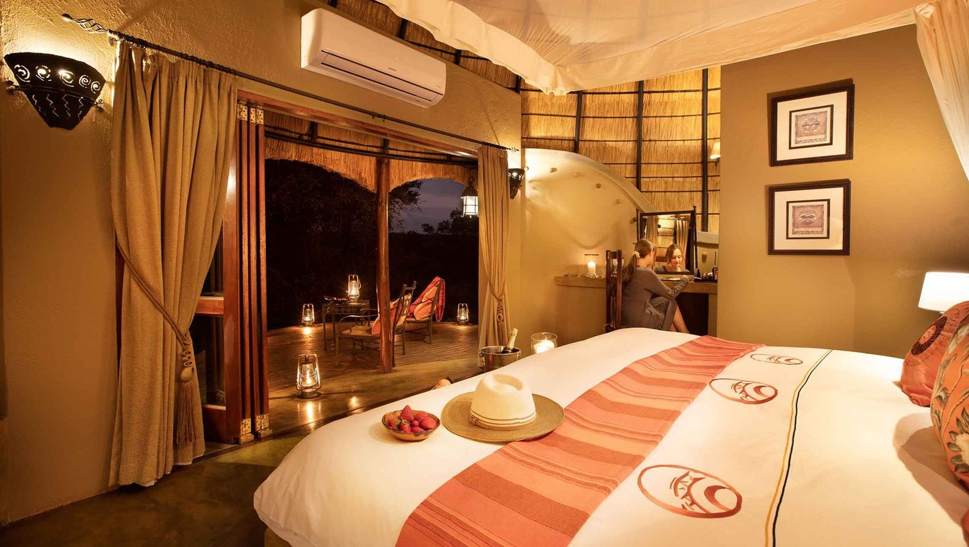 Bedroom with striped linens opening onto a private deck at Hoyo Hoyo Safari Lodge