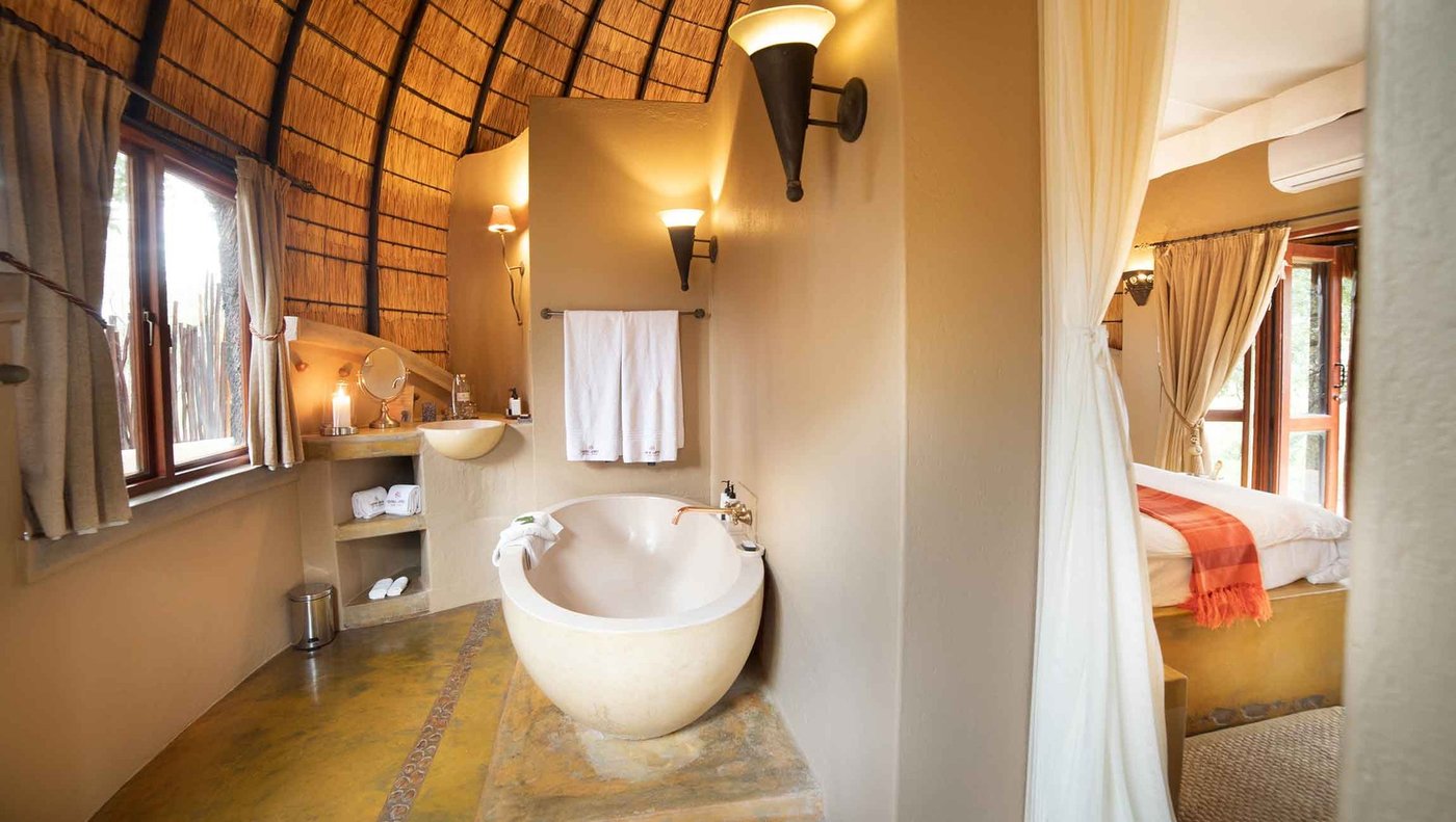 Round soaking tub and walk-in shower in a thatched bathroom at Hoyo Hoyo Safari Lodge