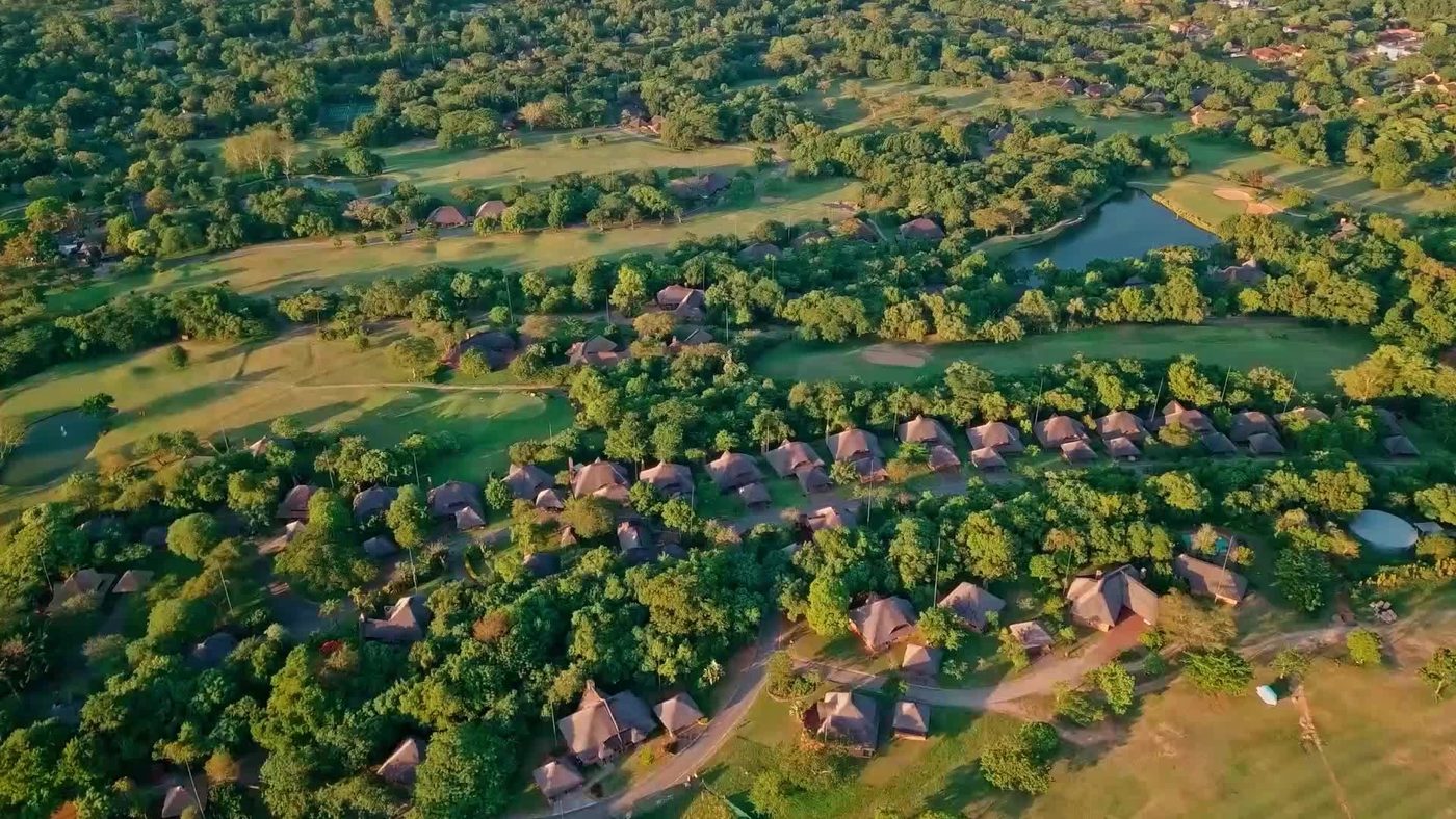 Aerial view of thatched chalets and golf course at Kruger Park Lodge in Kruger