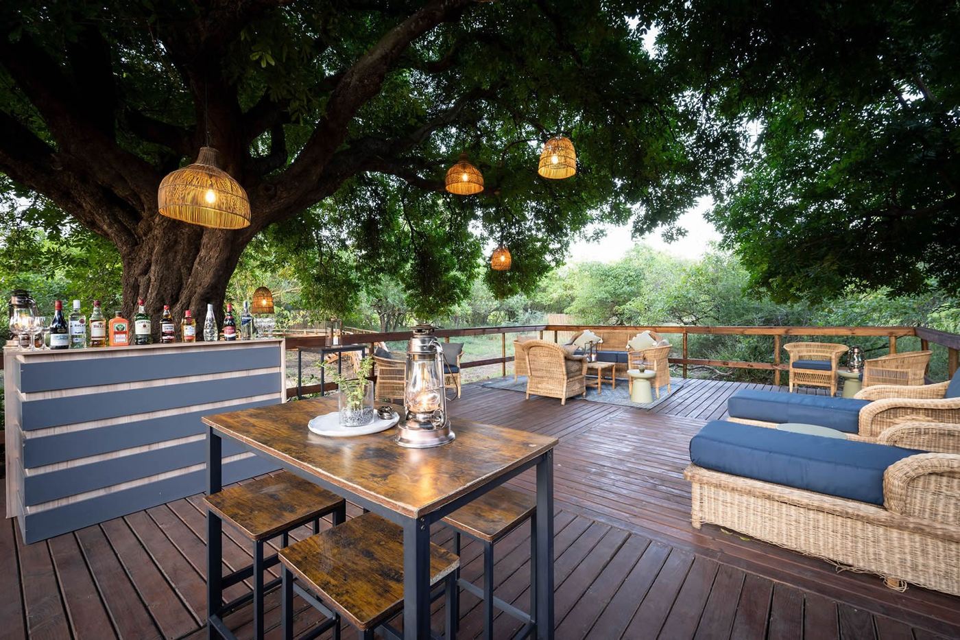 Communal dining deck strung with lanterns under a tree at Kruger Untamed Satara Plains Camp