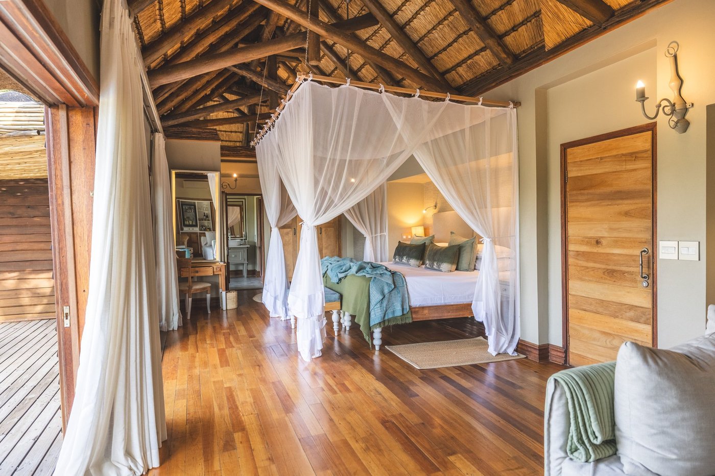 Open-sided bedroom with a canopy bed beneath a thatched roof at Lion Sands Narina Lodge