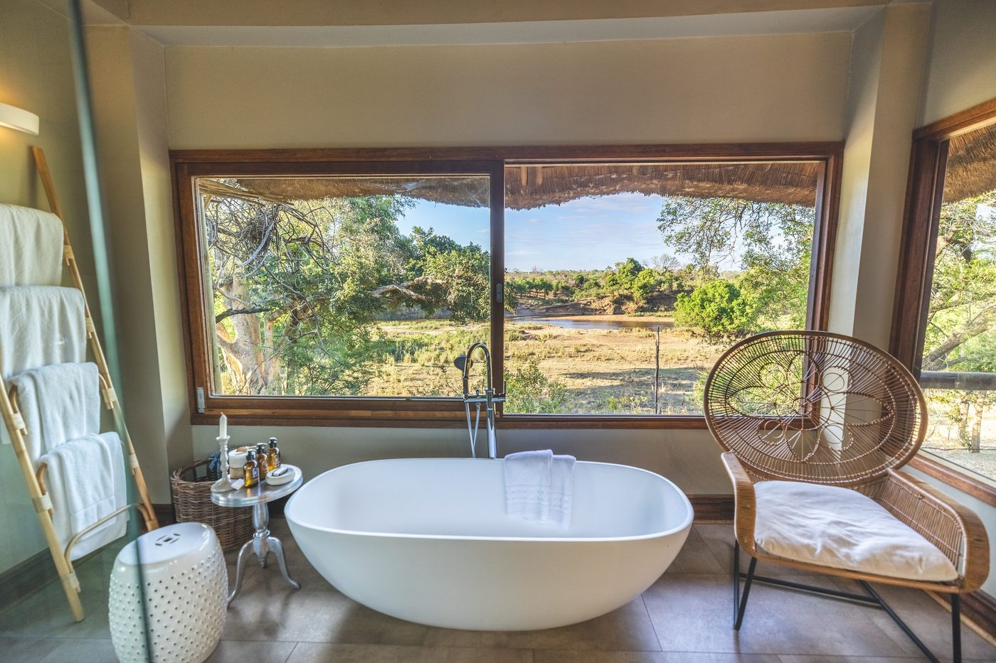 Freestanding bathtub beside floor-to-ceiling windows overlooking the bush at Lion Sands Narina Lodge