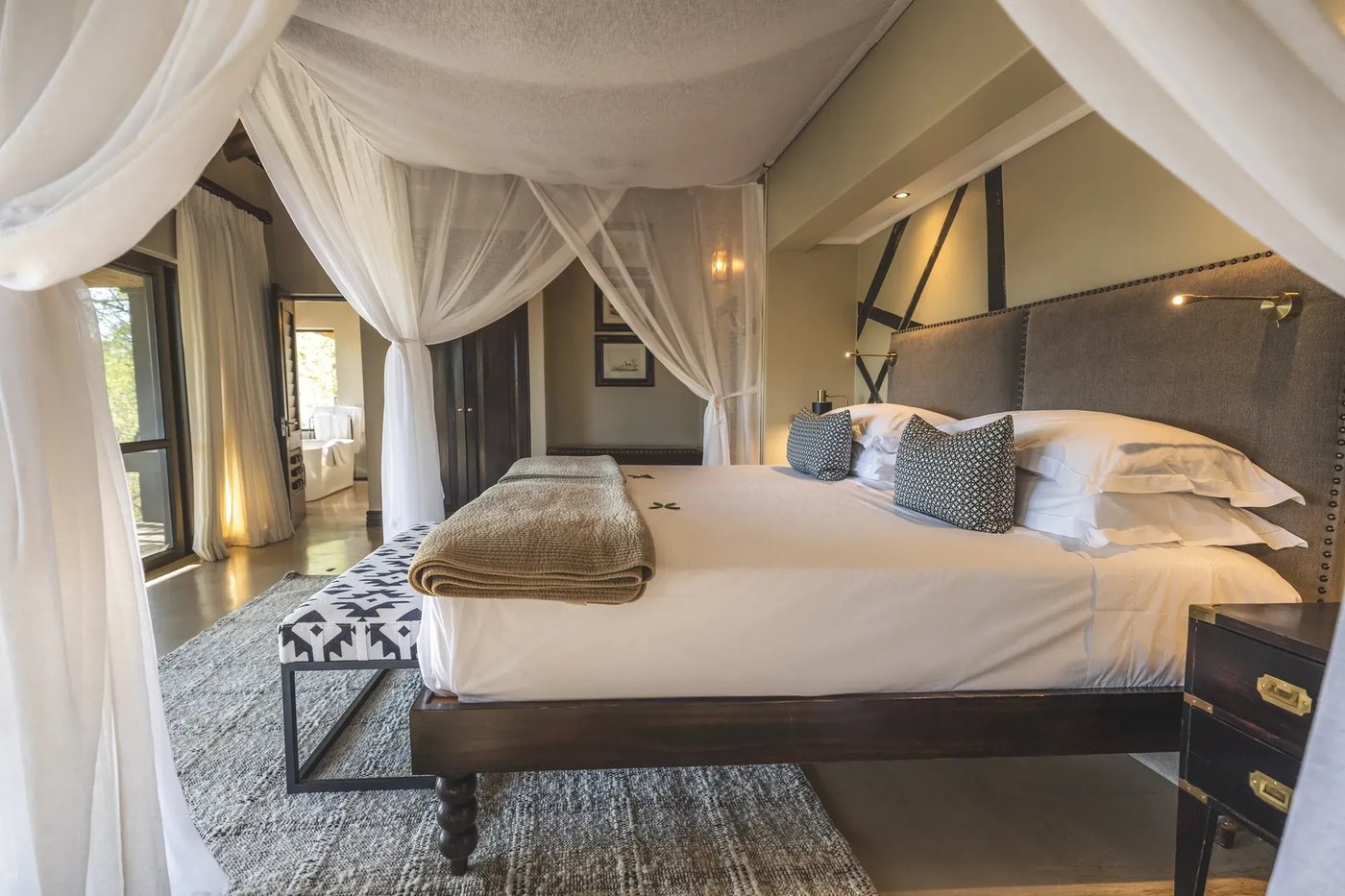 Canopy bed with a tufted headboard and bench at Lion Sands Tinga Lodge