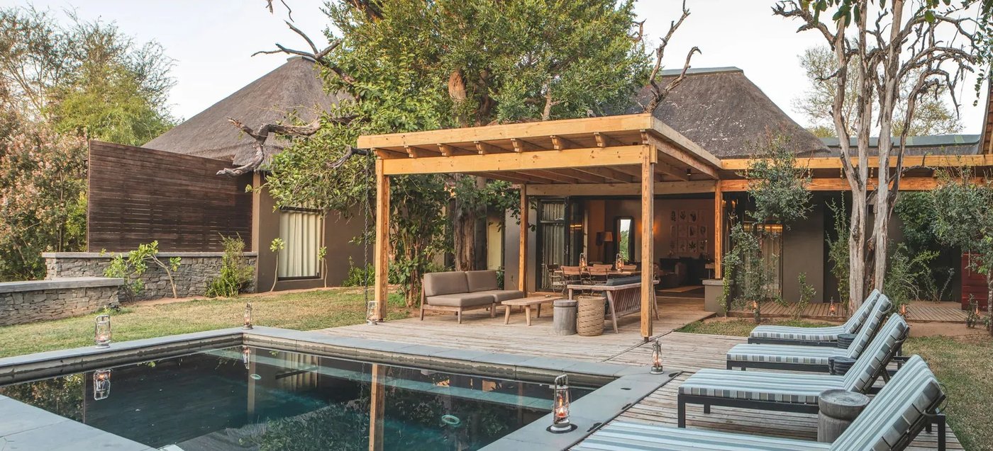 Pool deck with a wooden pergola and loungers at Lion Sands Tinga Lodge