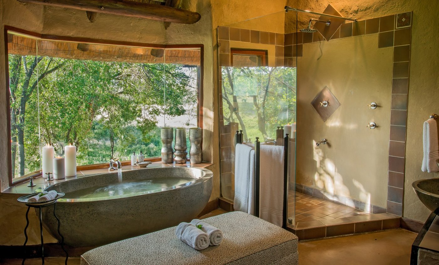 Freestanding tub beside a glass shower overlooking the forest at Lukimbi Safari Lodge