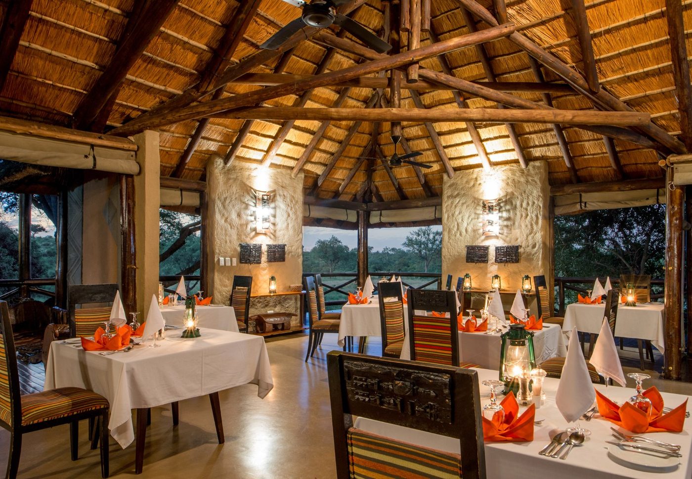 Thatched dining hall set for dinner at dusk at Lukimbi Safari Lodge