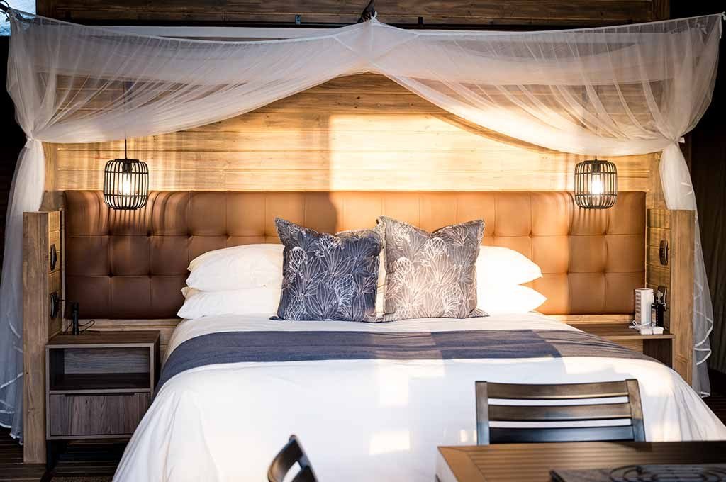 Canopy bed with tufted headboard in a tented suite at Nkuhlu Tented Camp
